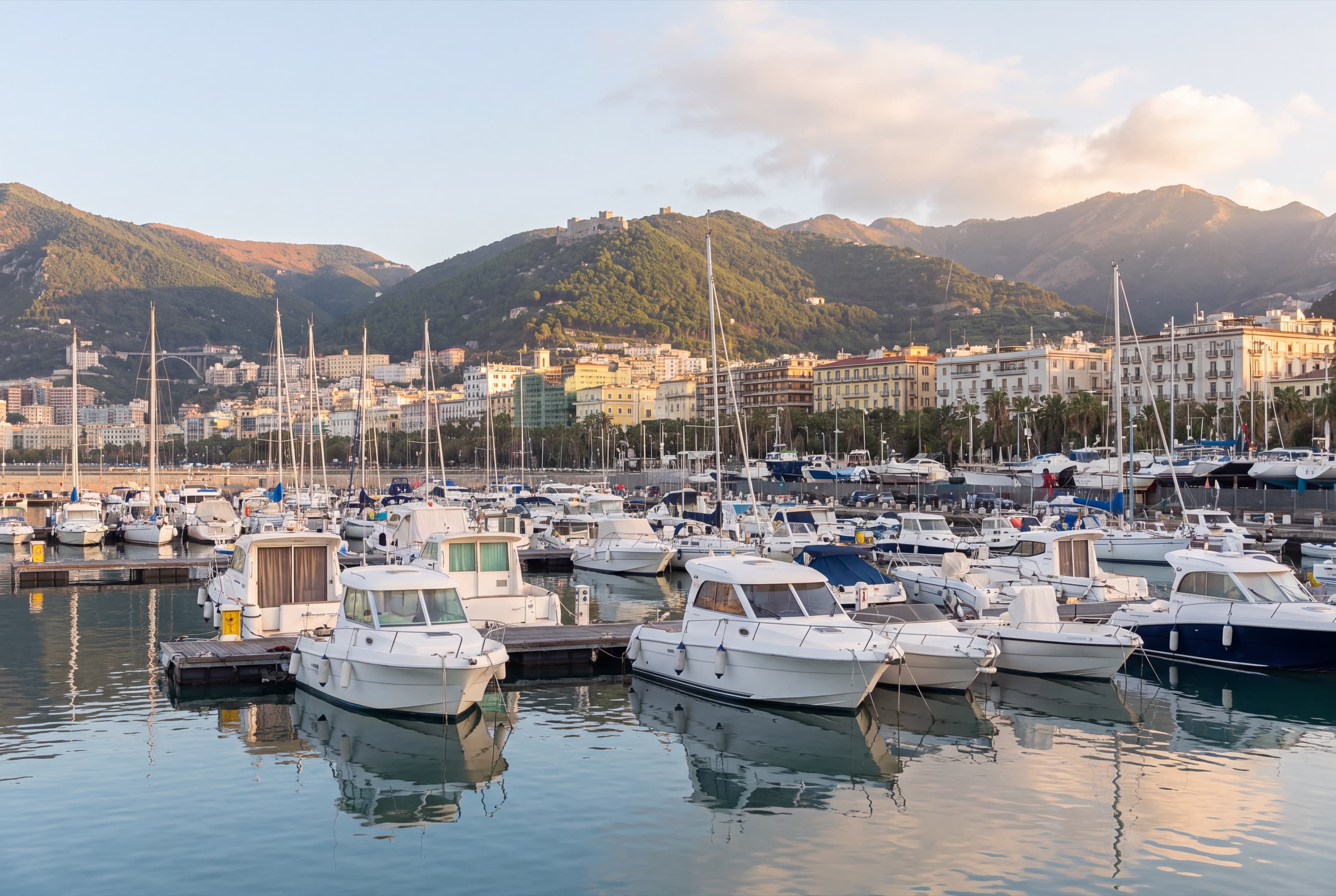 Motor boats and sailing boats in a marina of Salerno, with the city and the mountains behind