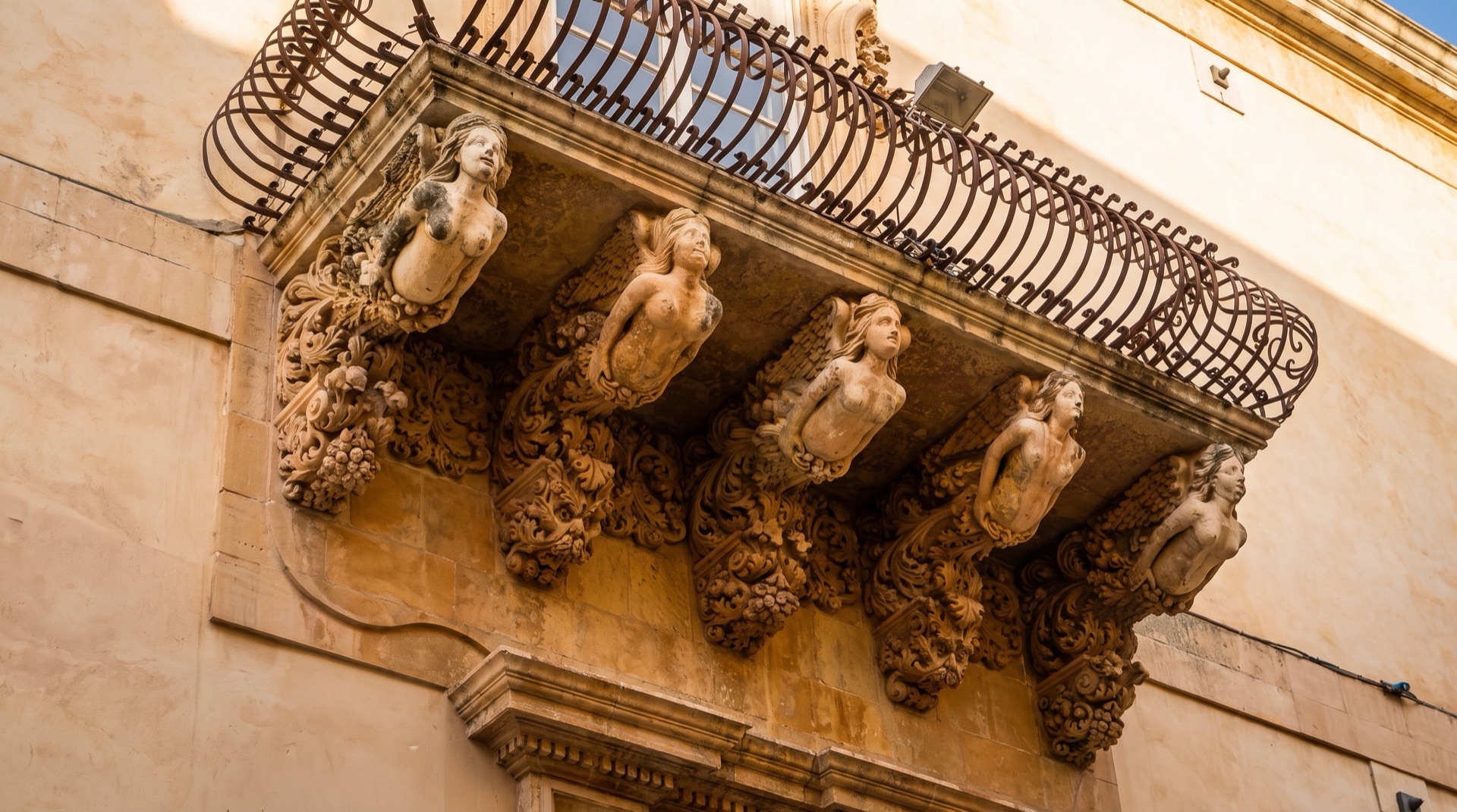 Carved stone balcony bracket on a Noto palace, the figurative detail that defines the late baroque of the Val di Noto