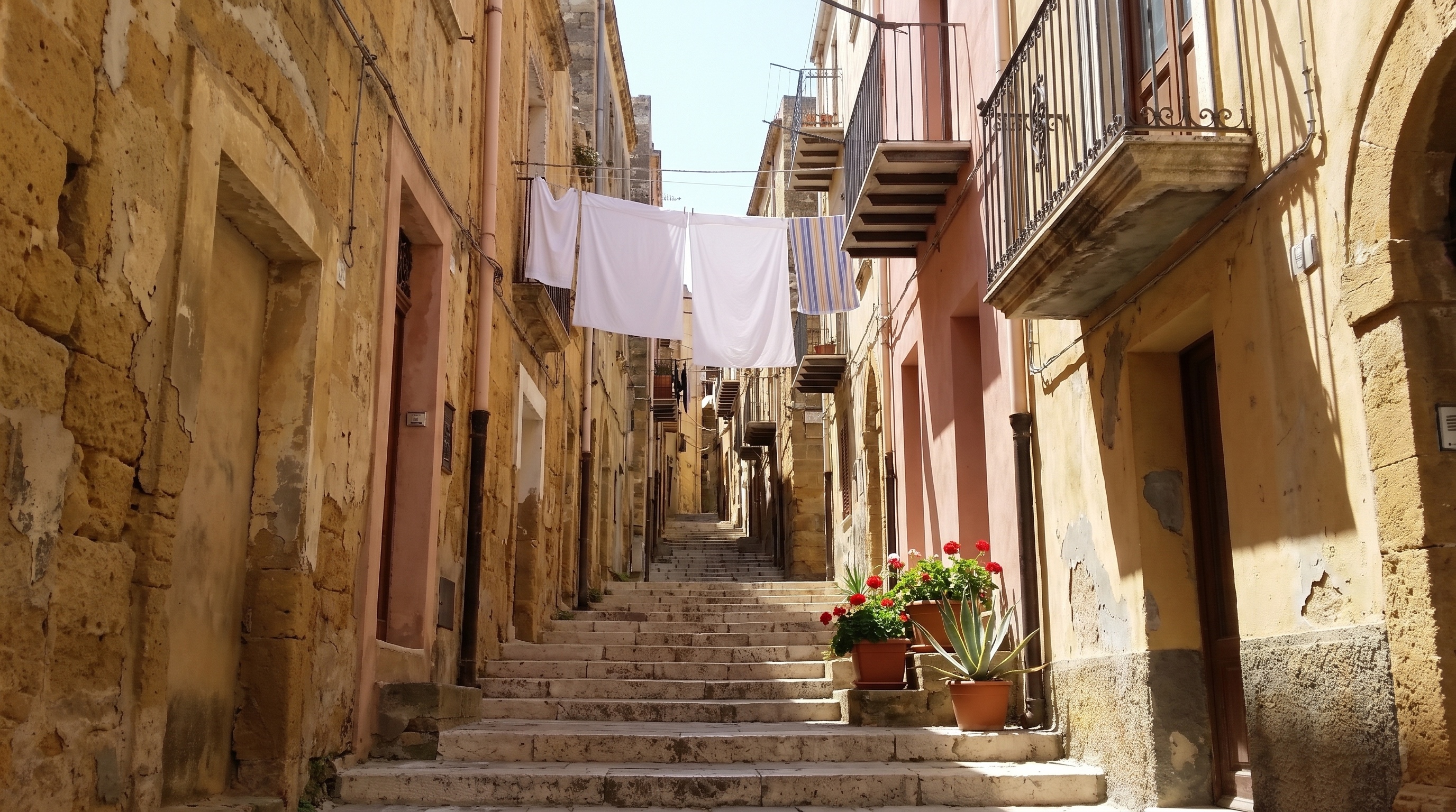 A steep uphill street in the old centre of Agrigento, between low sand-coloured buildings