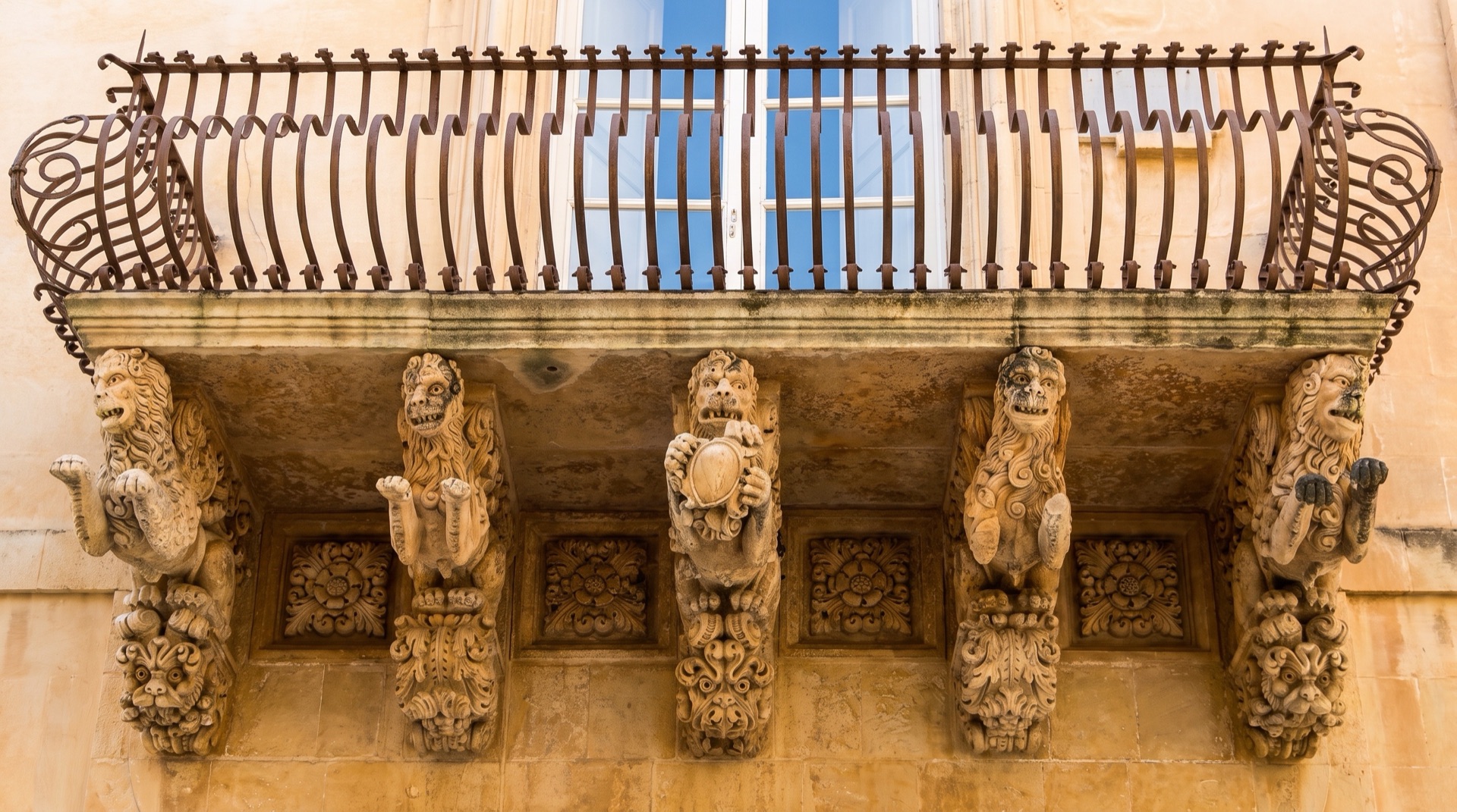 Wrought-iron baroque balcony on a pale limestone facade in the old streets of Ortigia, Siracusa